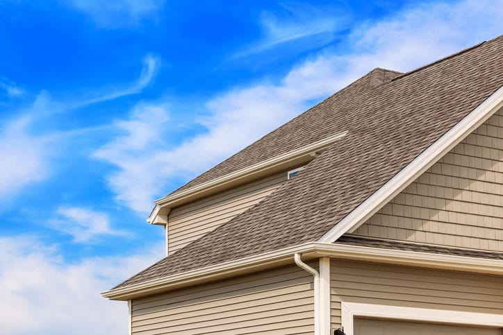 Photo of contemporary two story home showing a new asphalt roof,vinyl siding and new gutters. Blue sky is in the background.