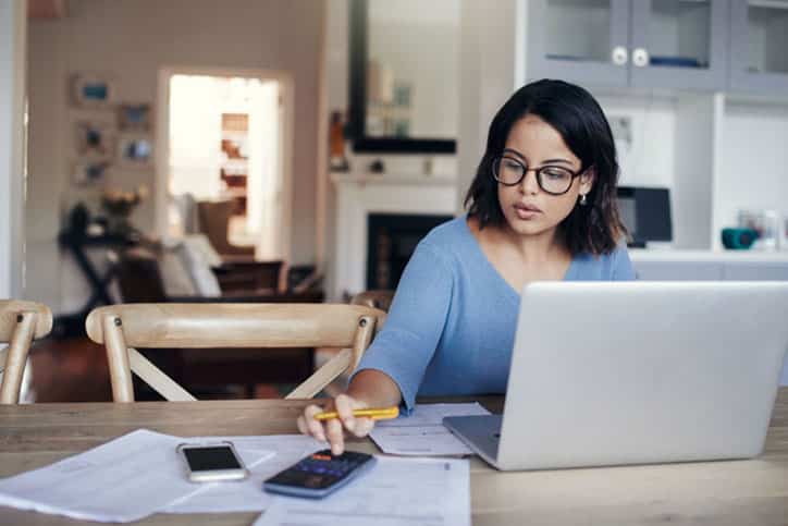 Shot of a young woman using a laptop and calculator while working from home